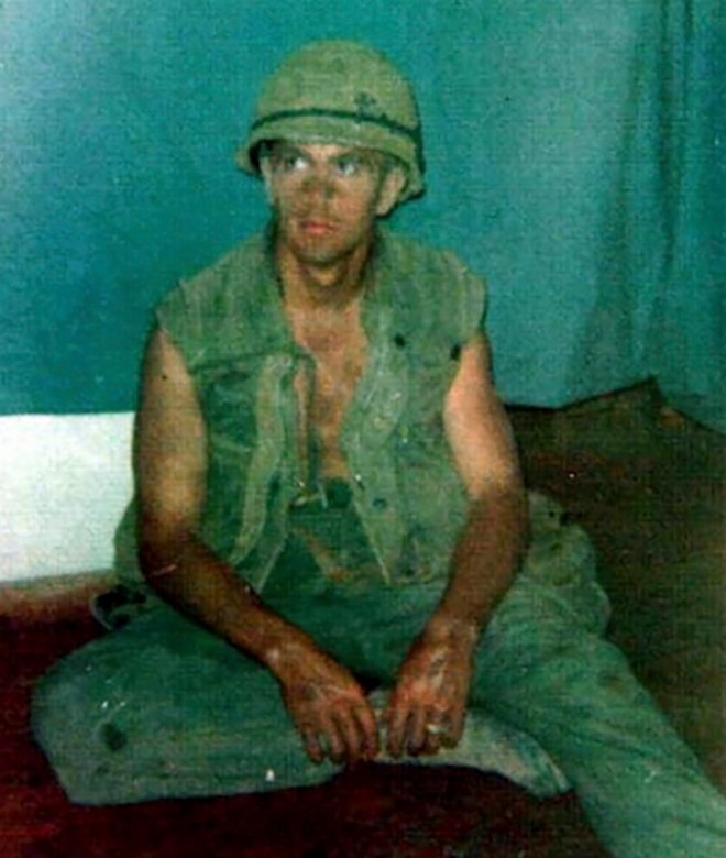 A man in combat uniform sits on a floor.