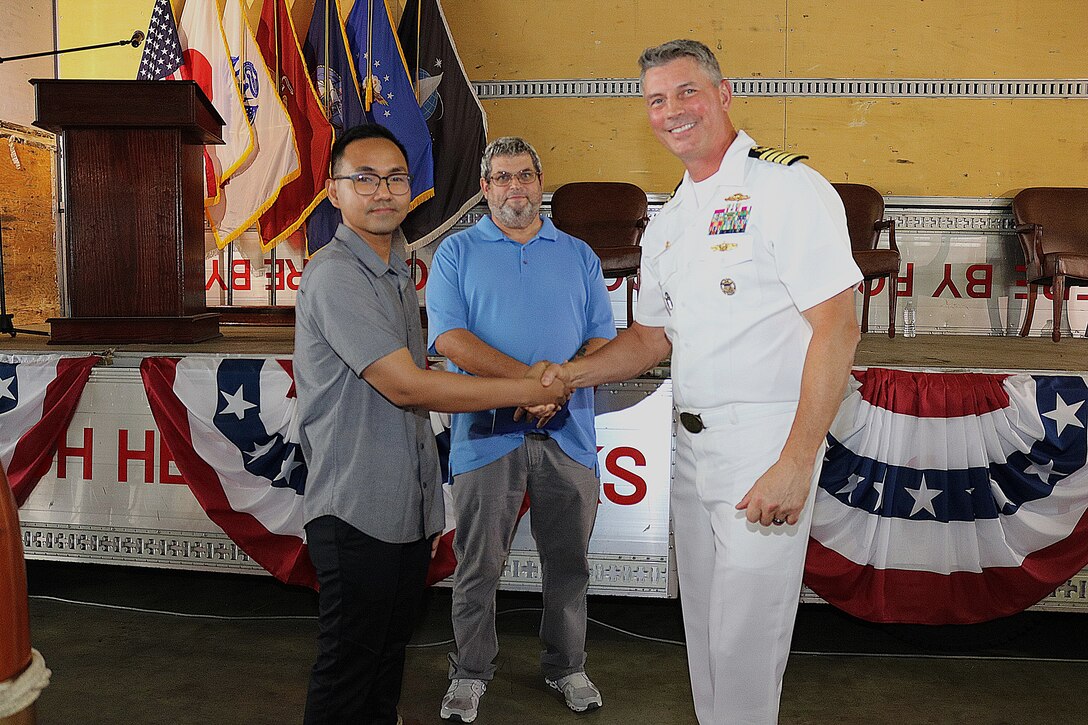 Two civilians, one shaking hands with a third person, a US Navy officer.