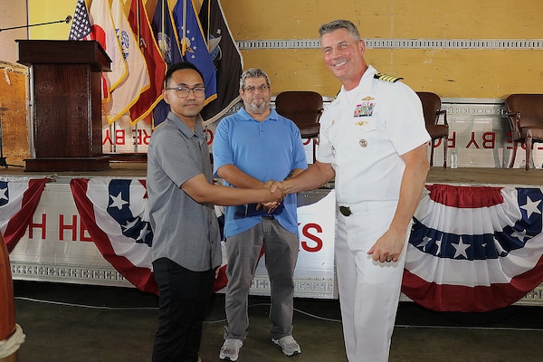 Two civilians, one shaking hands with a third person, a US Navy officer.