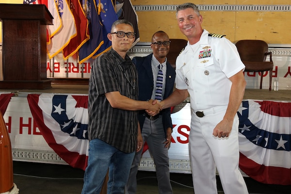Two civilians, one shaking hands with a third person, a US Navy officer.