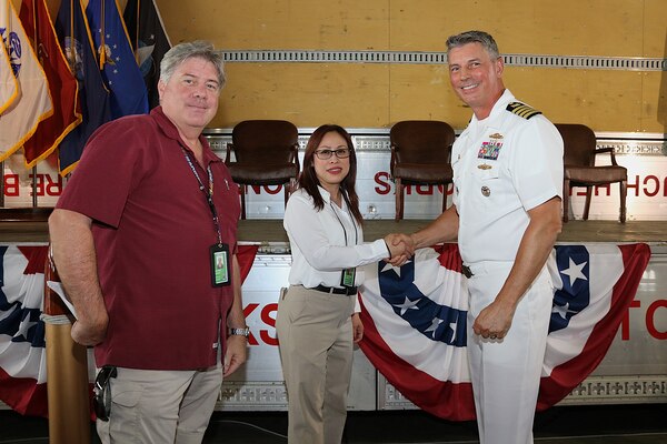 Two civilians, one shaking hands with a US Navy officer.