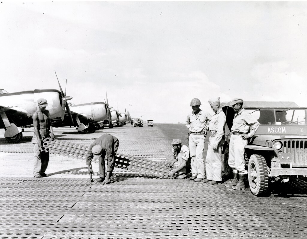 Construction of the critical Tanauan Airdrome, Leyte, Philippines, 16 December 1944. Men of the 1897th Engineer Aviation Battalion lay steel mat while commanding officer Col. James E. O'Keefe (left) and Maj. Gen. Hugh J. Casey (center) watch. 
Casey Papers, CEHO.