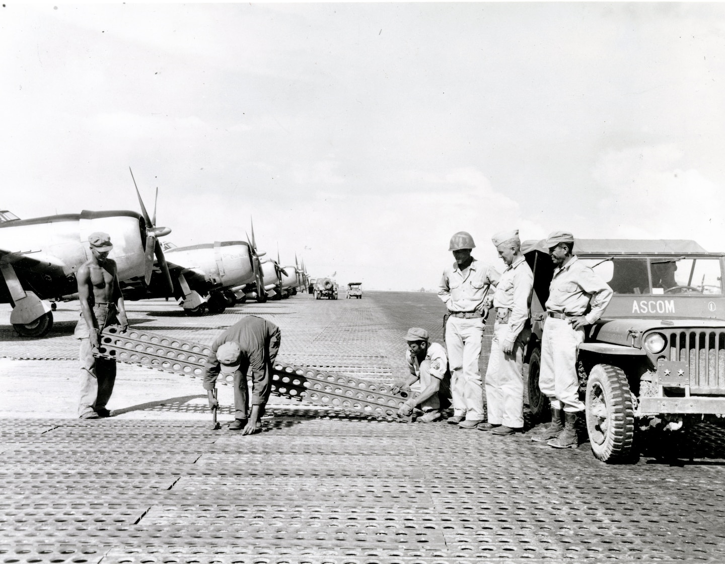 Construction of the critical Tanauan Airdrome, Leyte, Philippines, 16 December 1944. Men of the 1897th Engineer Aviation Battalion lay steel mat while commanding officer Col. James E. O'Keefe (left) and Maj. Gen. Hugh J. Casey (center) watch. 
Casey Papers, CEHO.