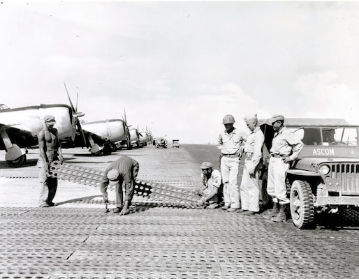 Construction of the critical Tanauan Airdrome, Leyte, Philippines, 16 December 1944. Men of the 1897th Engineer Aviation Battalion lay steel mat while commanding officer Col. James E. O'Keefe (left) and Maj. Gen. Hugh J. Casey (center) watch. 
Casey Papers, CEHO.