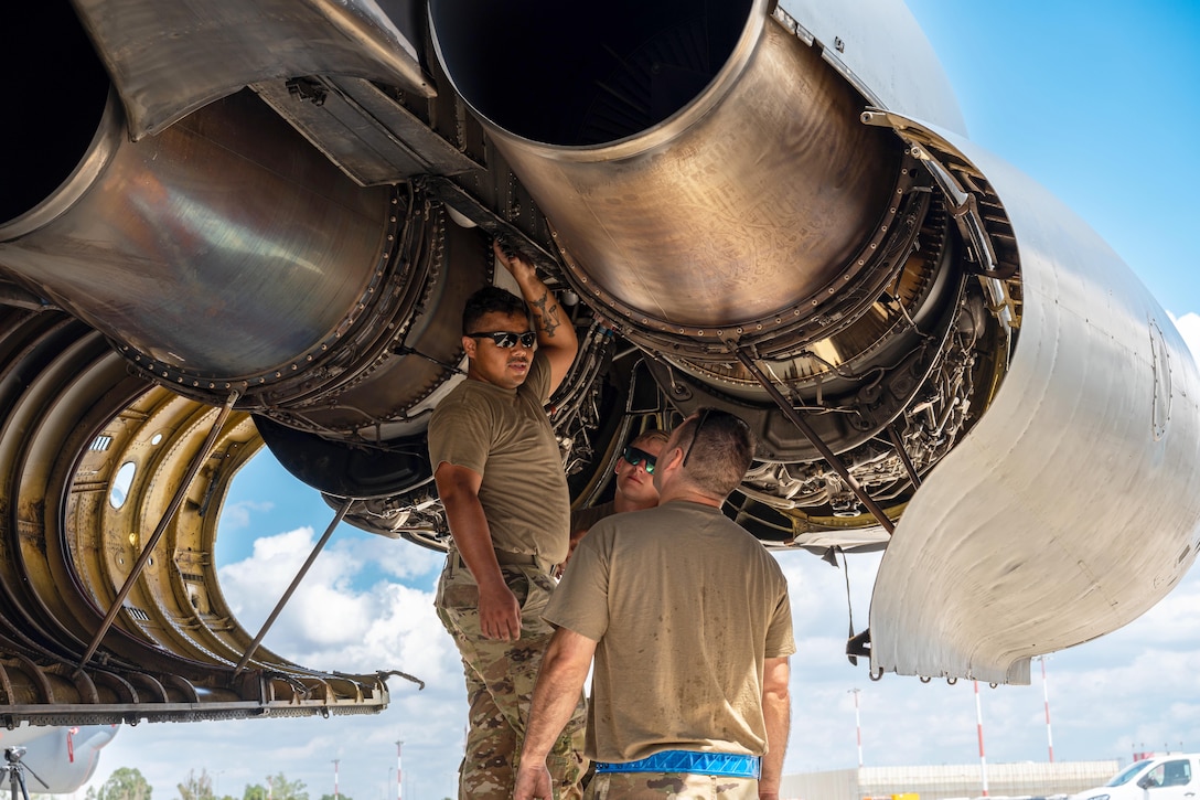 Three airmen talk while working on an aircraft's engine.