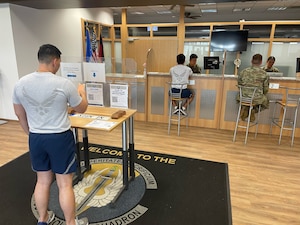 An Airmen scans a QR code at a table for an appointment with comptroller while others are waited on in background