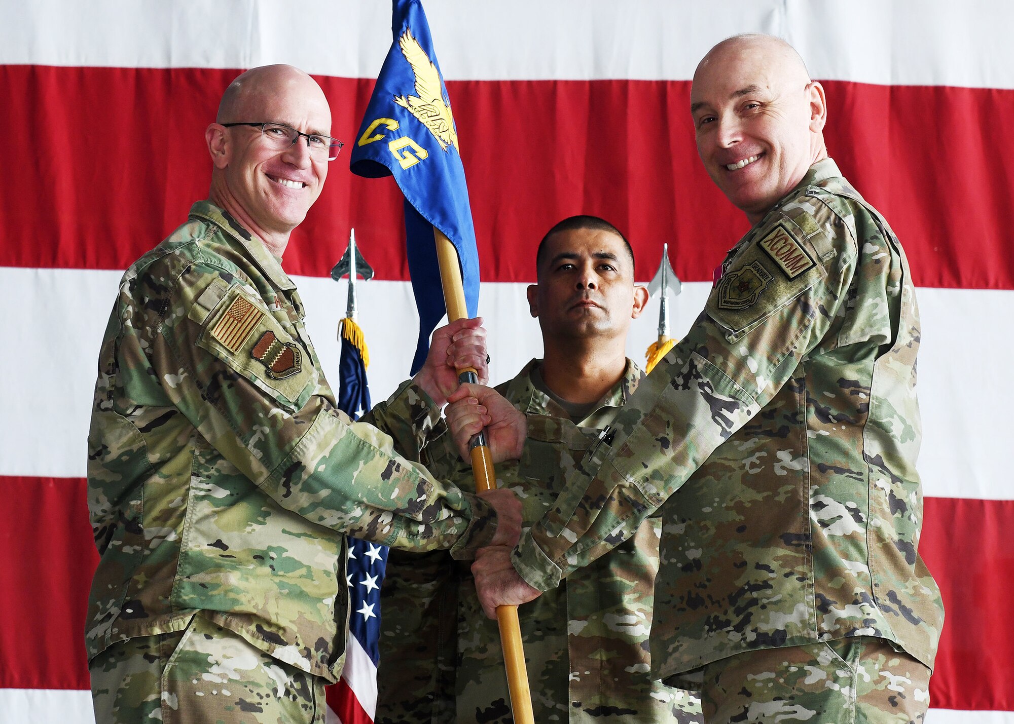 two uniformed men hold guidon together while posing for photo.