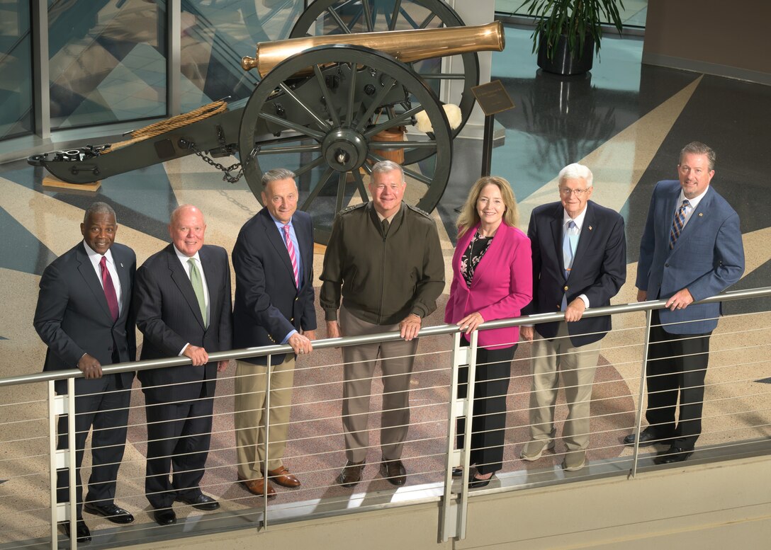 Seven men and one woman stand in front of a hand railing