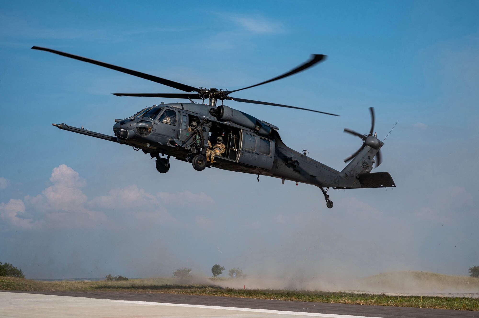 A helicopter flies close to the ground, kicking up dirt