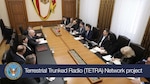 Conference table with officials from DTRA, Moldova's MIA, and US Embassy. Wood table, people seated on both sides. Blue banner shows DTRA seal and 'Terrestrial Trunked Radio Network project'.