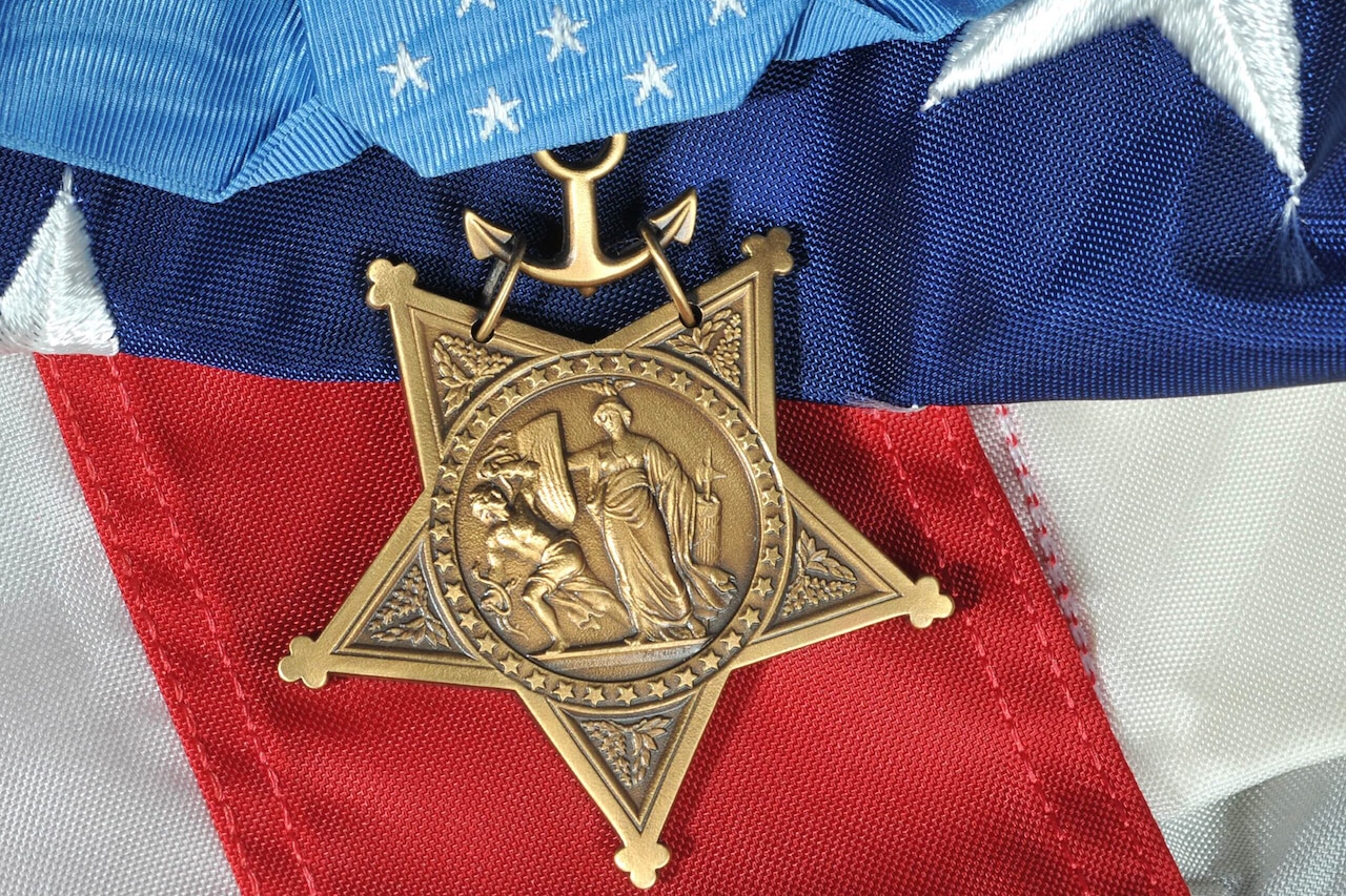 A photograph shows a military metal resting on a stars and stripes background.