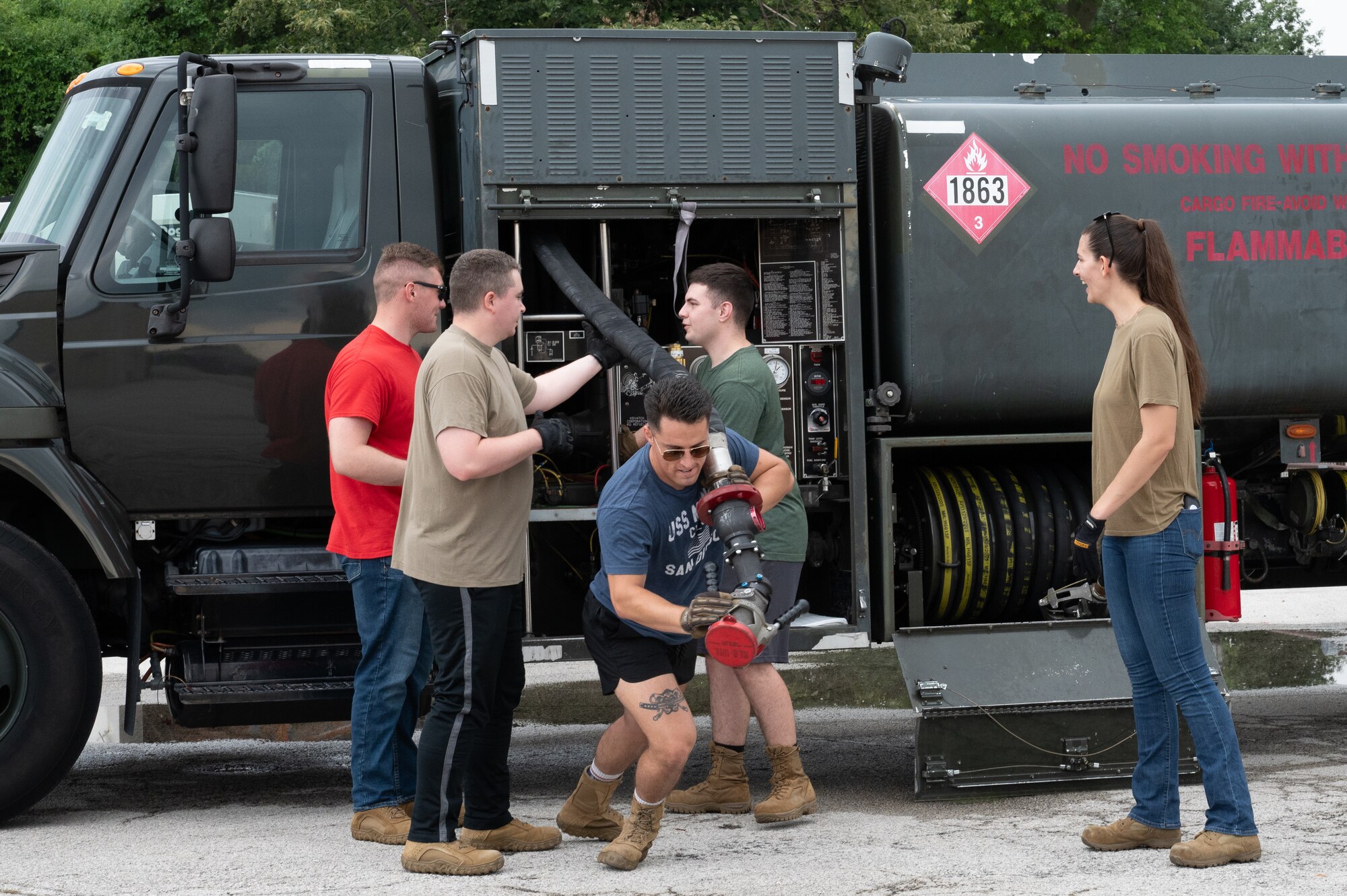 An Airman begins to drag a hose away from its holster as other Airman help uncurl it.