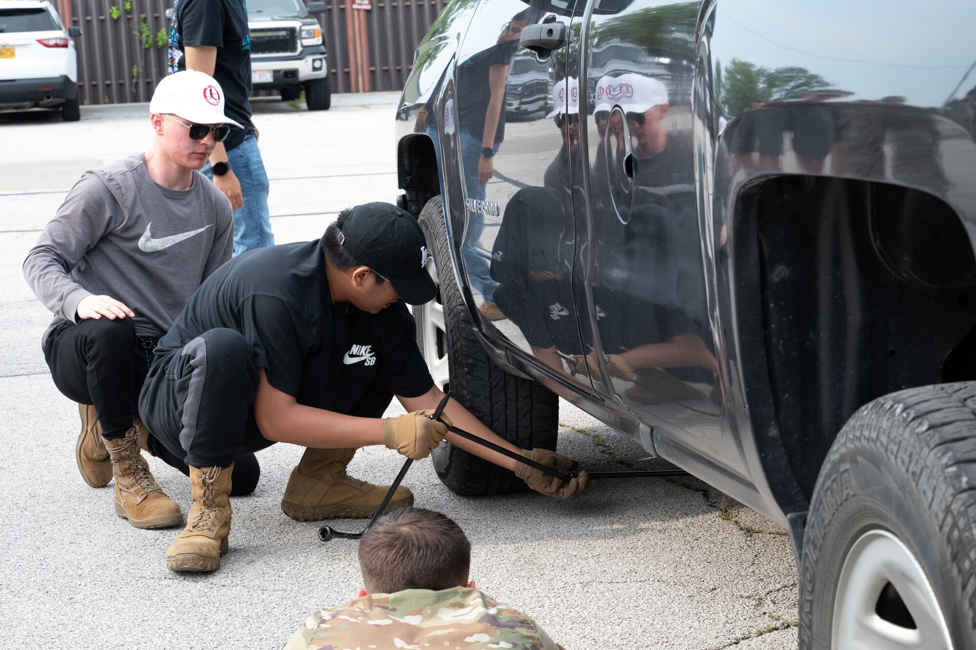 An Airman lifts a truck to change its tire as other airman kneel around him.