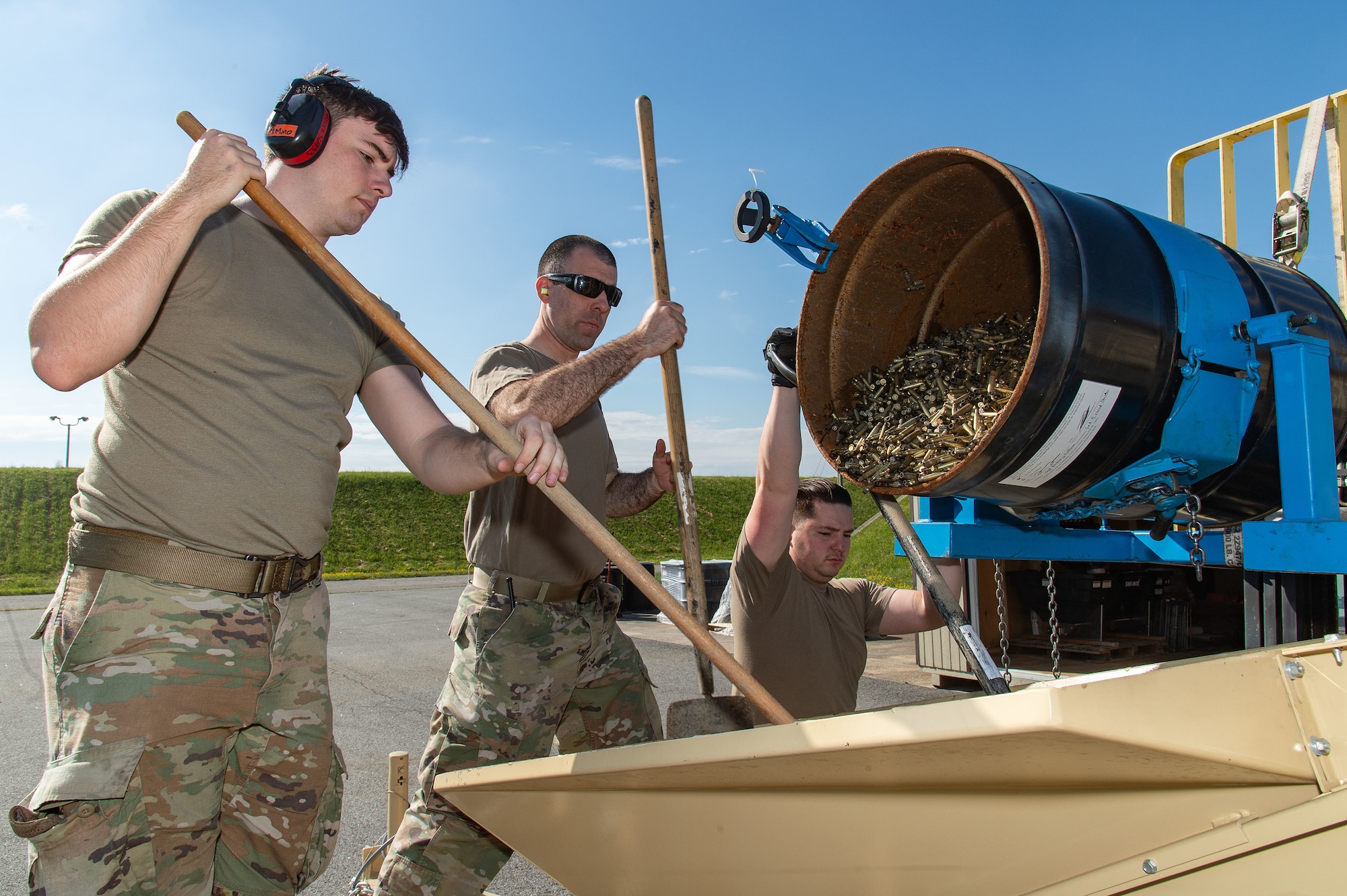U.S. Air Force Senior Airman Brian Rice, left, 436th Maintenance Squadron munitions crew chief; Tech. Sgt. Zachary Huffman, center, 436th MXS senior munitions inspector; and Senior Airman Nathaniel Weikert, right, 436th MXS munitions crew chief, load spent small caliber brass munition cartridges into a deformer at Dover Air Force Base, Delaware, May 1, 2024. From its first use in February 2019, proceeds from brass sales have paid for the deformer and are now generating revenue for the base. (U.S. Air Force photo by Roland Balik)