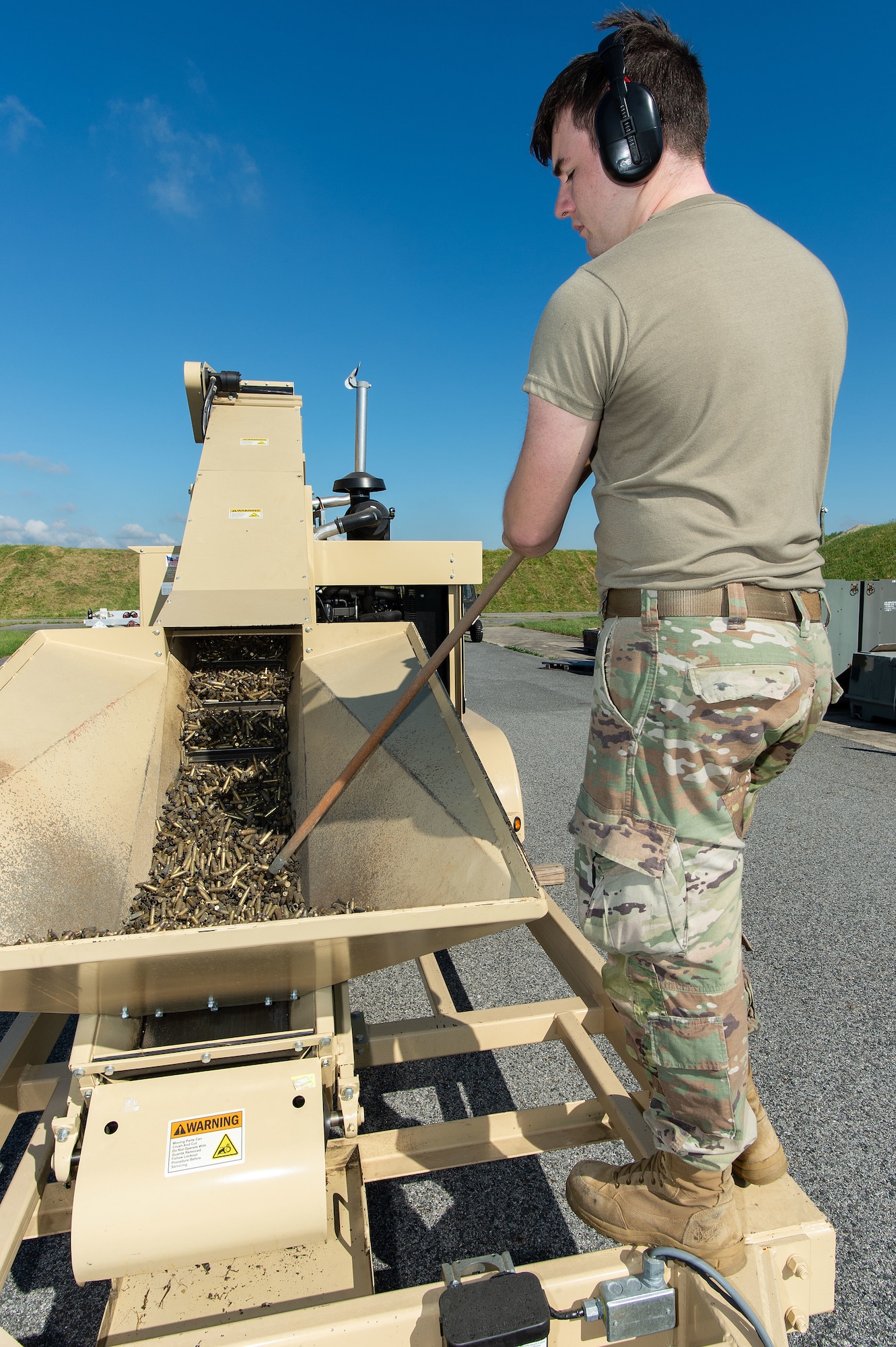 U.S. Air Force Senior Airman Brian Rice, 436th Maintenance Squadron munitions crew chief, guides spent small caliber brass munition cartridges on the deformer conveyor at Dover Air Force Base, Delaware, May 1, 2024. From its first use in February 2019, proceeds from brass sales have paid for the deformer and are now generating revenue for the base. (U.S. Air Force photo by Roland Balik)