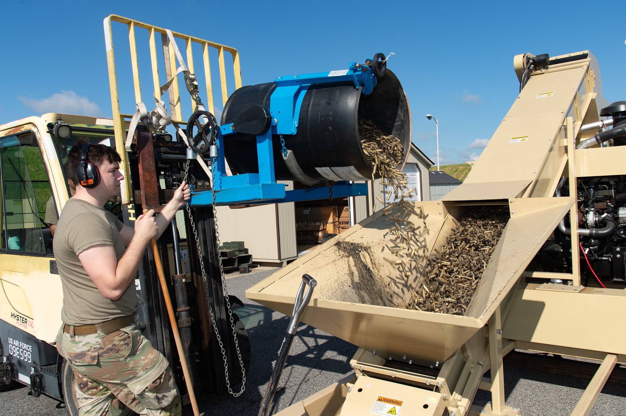 U.S. Air Force Senior Airman Brian Rice, 436th Maintenance Squadron munitions crew chief, dumps small caliber brass munition cartridges into the deformer to be demilitarized at Dover Air Force Base, Delaware, May 1, 2024. From its first use in February 2019, proceeds from brass sales have paid for the deformer and are now generating revenue for the base. (U.S. Air Force photo by Roland Balik)