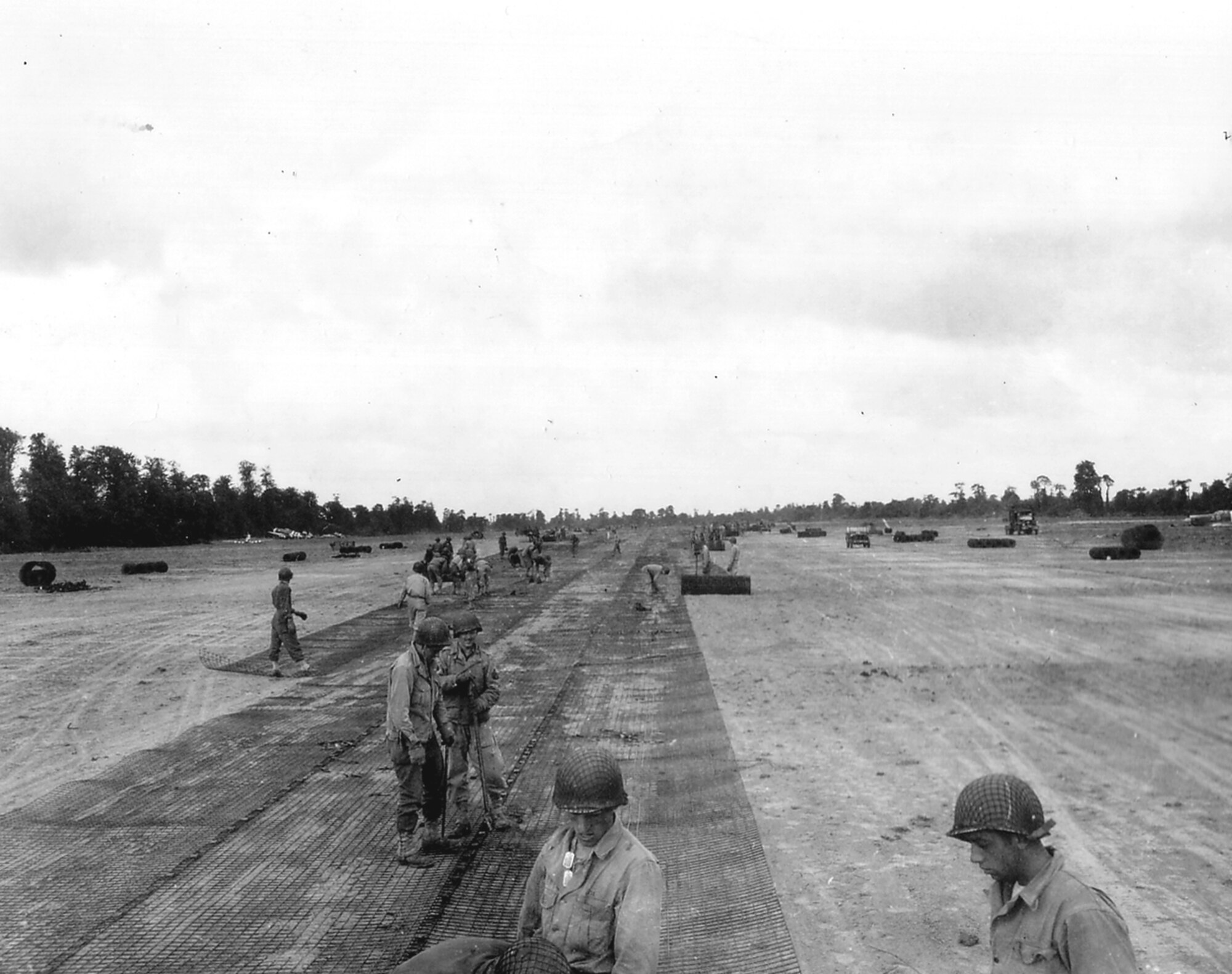 Advanced Landing Ground A-6 near Sainte Mère Eglise, France was one of the first ALG’s to be established in Normandy after D-Day. Pictured here on/about June 14, 1944, soldiers of the U.S. Army 819th Engineer Aviation Battalion lay Square Mesh Track for the runway in La Londe (Beuzeville-au-Plain). In the left distance lie several derelict fighter aircraft which made emergency landings on the airfield grounds. They include a P-47 Thunderbolt from an unidentified unit and a pair of Spitfires, believed to belong to US Navy squadron VC-7 which used the aircraft to spot the fire of warships supporting the landings. (US Army photo via Flickr)