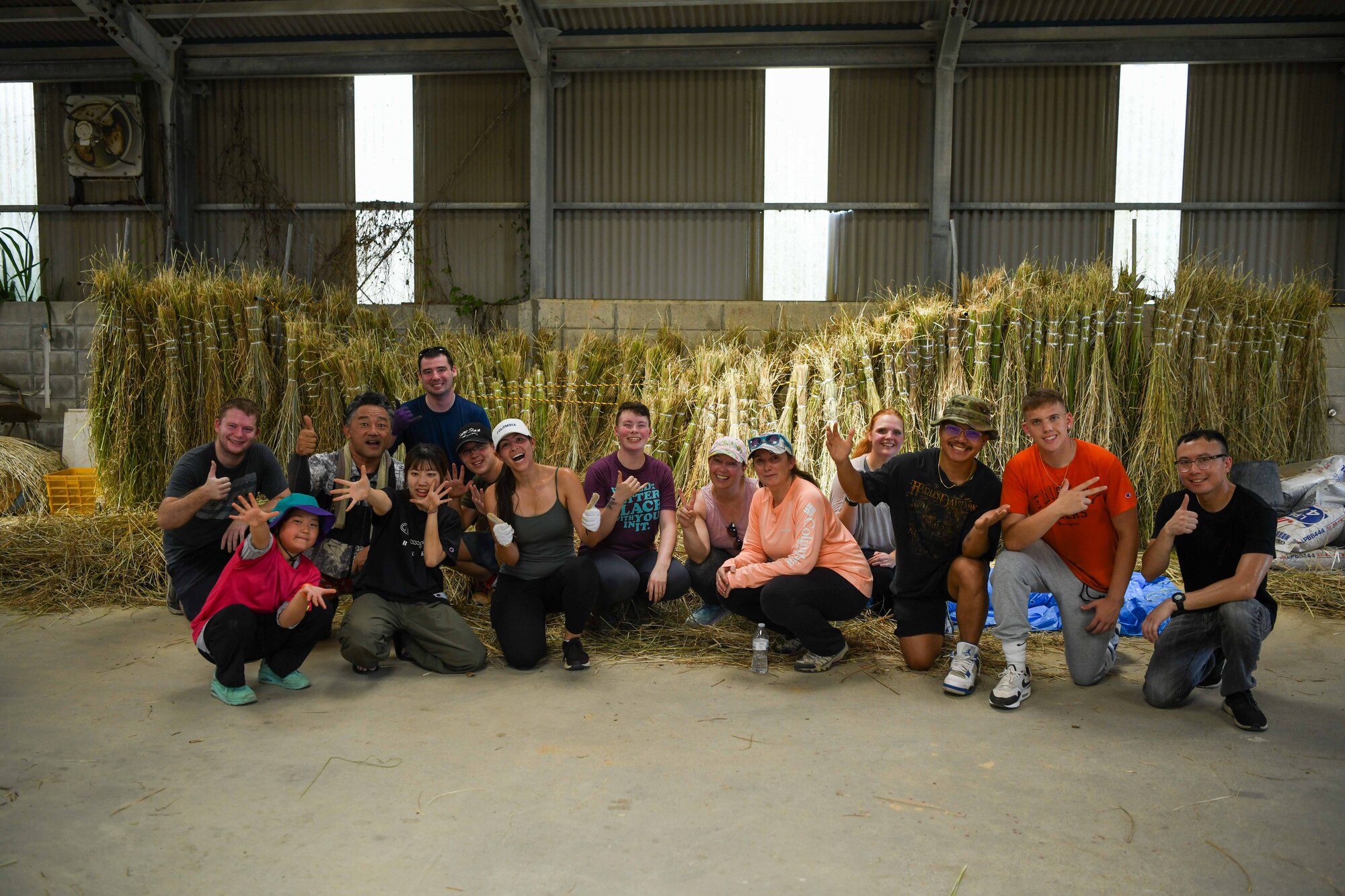 A group of military members and Okinawa locals pose for a photo in front of bundles of vetiver.
