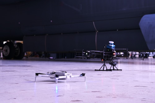 Two drones sit side by side and are placed in front of an aircraft