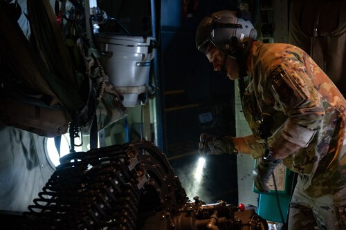 Airman with helmet shines flashlight through small cloud of smoke while inspecting large gun aboard plane