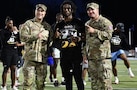 Men in Army uniform pose for photo with clinic participant on football field.