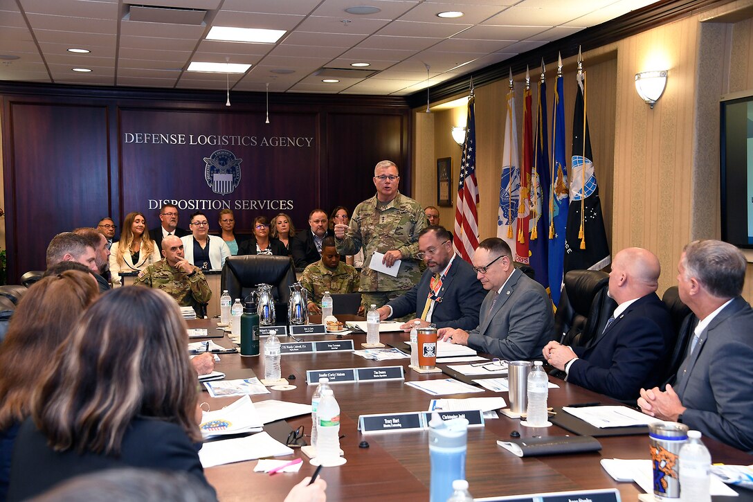 A general speaks to a group of employees sitting around a conference table.
