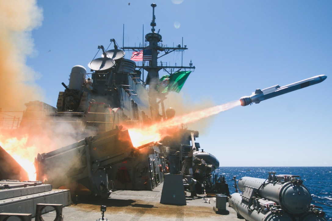 A missile fires from a ship at sea, creating a fireball as an American flag is displayed in the background.