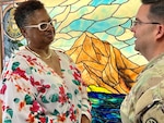 Woman speaking to the hospital Chaplain in front of a stained-glass window.