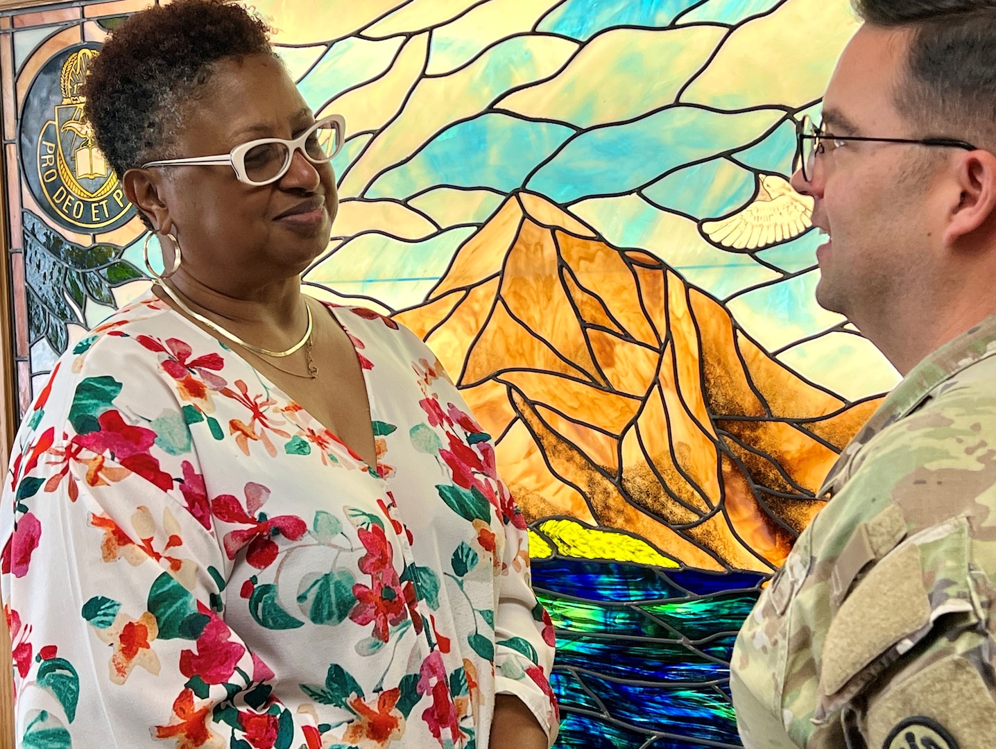 Woman speaking to the hospital Chaplain in front of a stained-glass window.