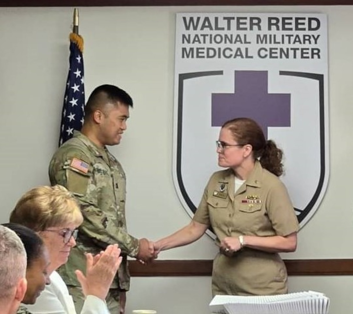 Army Capt. Mark DeJesus (left), an Emergency Department registered nurse, is recognized and congratulated by Walter Reed Director U.S. Navy Capt. (Dr.) Melissa Austin (right) and the rest of the Walter Reed Board of Directors during a BoD meeting on July 16. DeJesus is credited with providing life-saving care to an infant left in a vehicle parked off base on June 30 when temperatures were in the 90s.