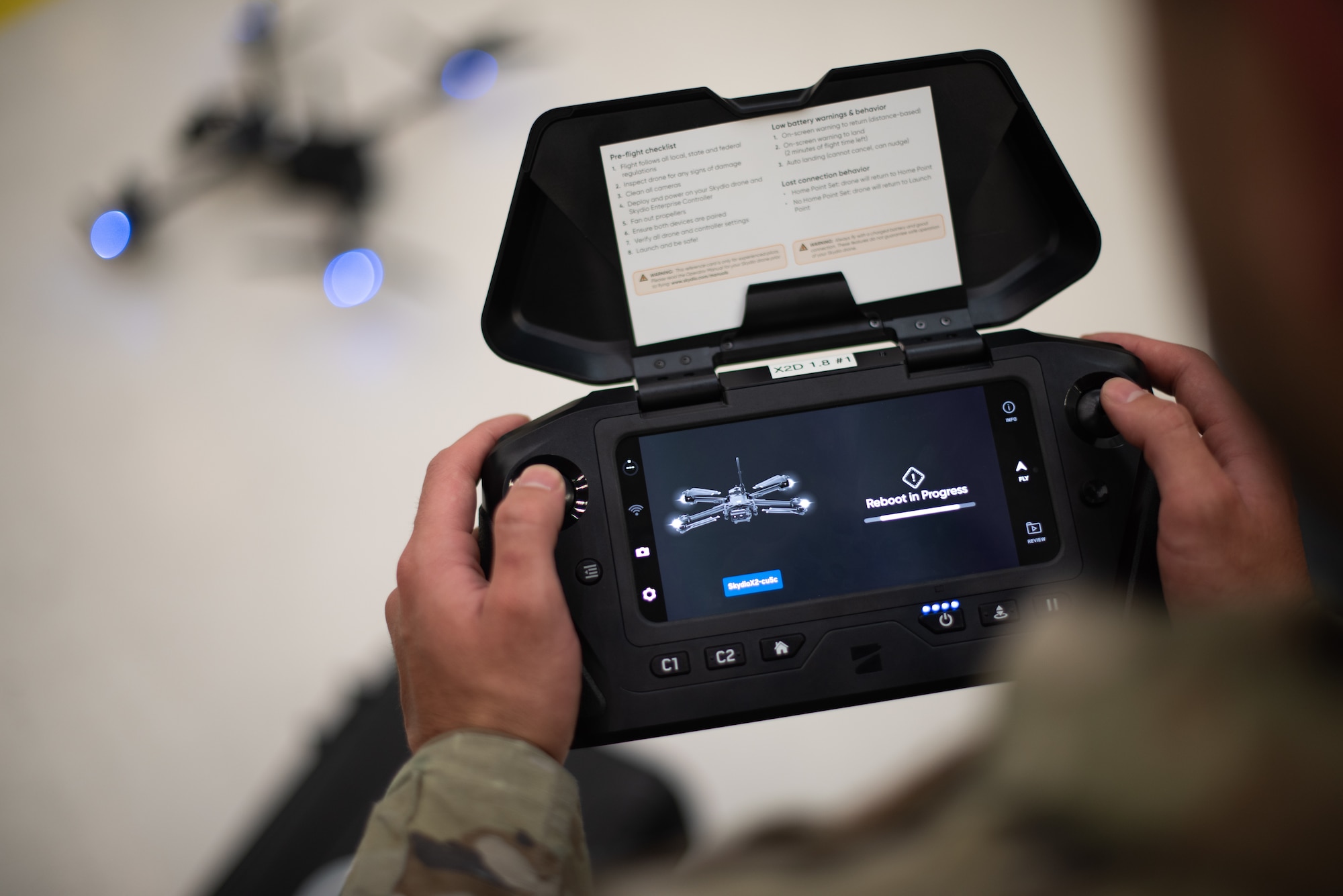 A drone controller is in an airman's hands with a drone out of focus in the background