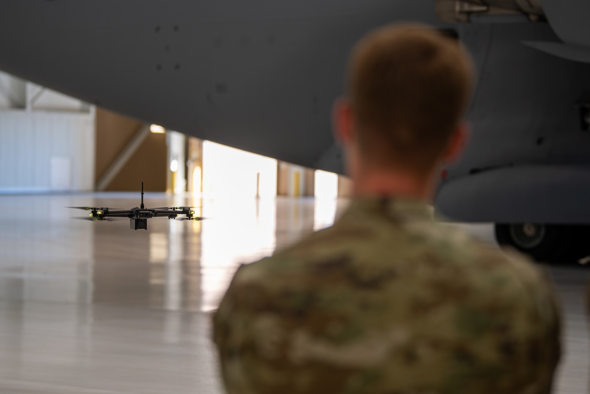 A drone hovers over the shoulder of an airman in the foreground