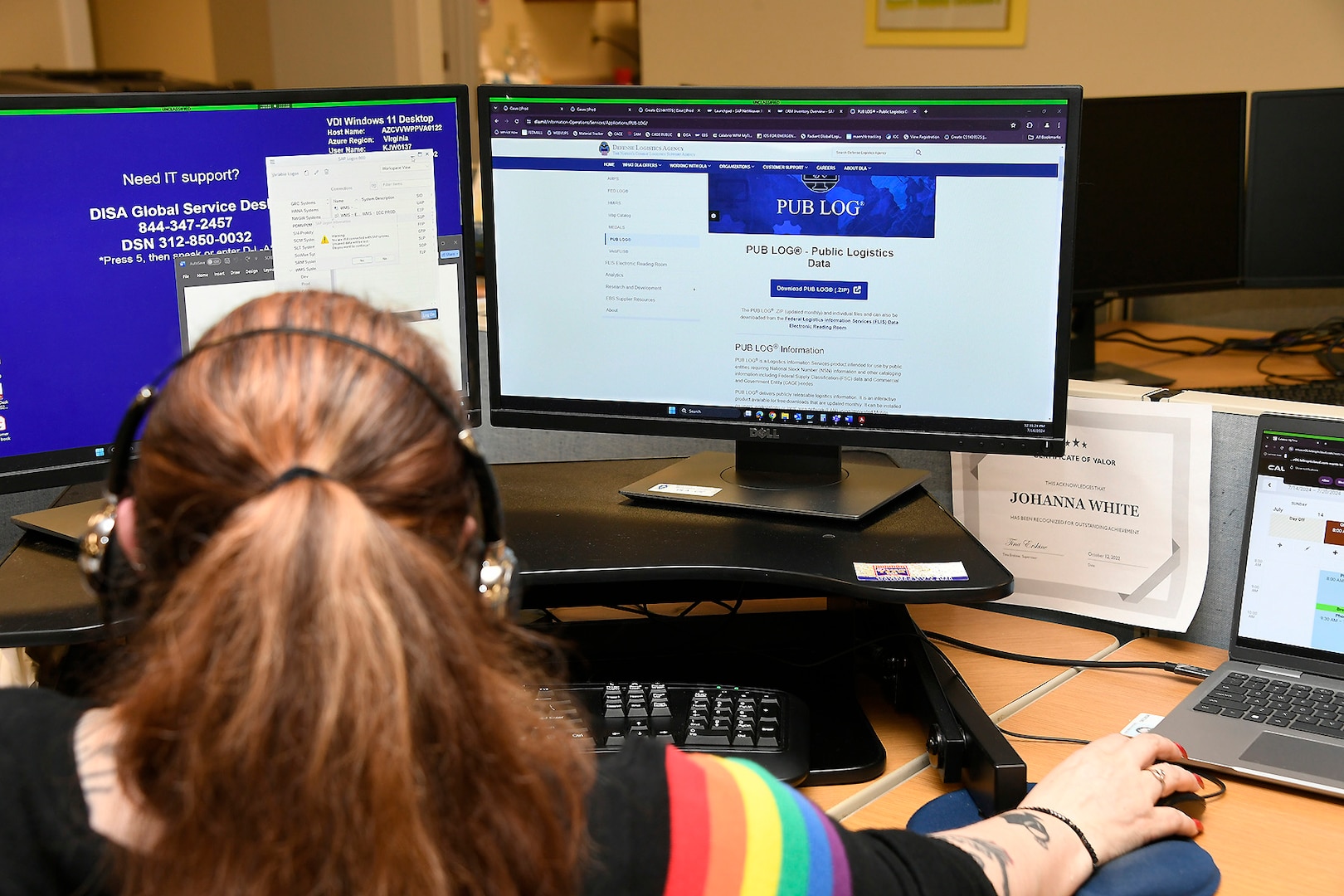 The back of the head of a woman wearing headphones in front of a computer monitor