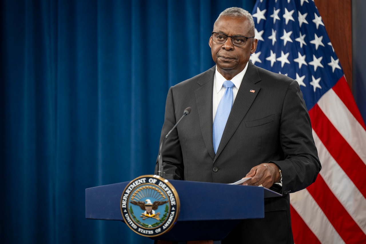 A man wearing a business suit stands at a lectern.