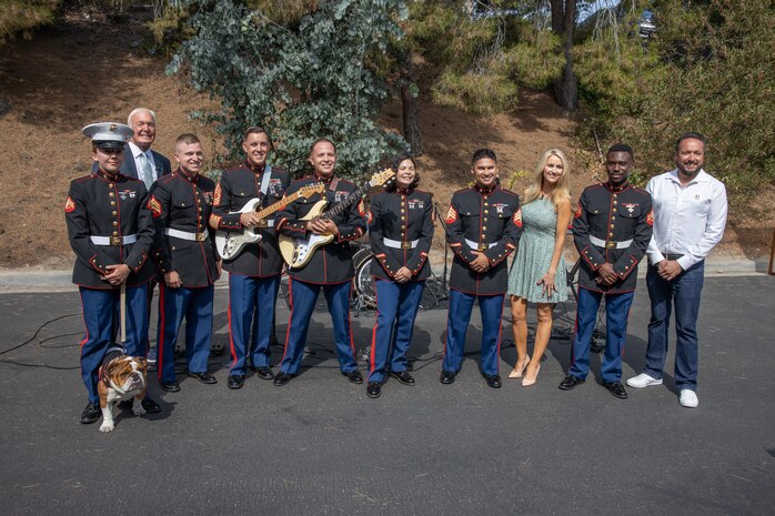 U.S. Marine Corps Cpl. Sarah Grawcock, a combat photographer and mascot handler, with Headquarters and Service Battalion, Marine Corps Recruit Depot San Diego, and Pfc. Bruno, the mascot of MCRD San Diego, Western Recruiting Region, left, pose for a photo with Marine Band San Diego and members of KUSI-TV at KUSI-TV television station San Diego, July 10, 2024. The mascot's and Marine Band San Diego’s job is to boost morale, participate in outreach work and attend events and ceremonies. The Marine Band San Diego participated in a live news performance and interview to help promote their neighborhood activation concert in Little Italy. (U.S. Marine Corps photo by Capt. Austin Gallegos)