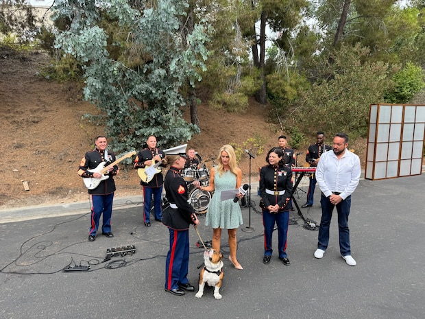 U.S. Marine Corps Cpl. Sarah Grawcock, a combat photographer and mascot handler, with Headquarters and Service Battalion, Marine Corps Recruit Depot San Diego, Pfc. Bruno, the mascot of MCRD San Diego, Western Recruiting Region, speak on live TV with Marine Band San Diego and members of KUSI-TV at KUSI-TV television station San Diego, July 10, 2024. The mascot's and Marine Band San Diego’s job is to boost morale, participate in outreach work and attend events and ceremonies. The Marine Band San Diego participated in a live news performance and interview to help promote their neighborhood activation concert in Little Italy. (U.S. Marine Corps photo by Capt. Austin Gallegos)