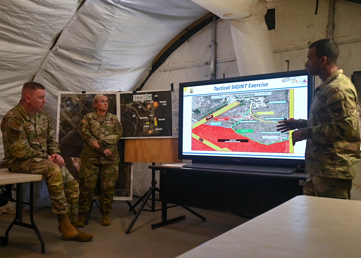 U.S. Air Force Chief Master Sgt. Chad Bickley, command chief for Air Education Training Command command, left, listens to a mission brief on the Joint All Domain Exercise Forward Operations Readiness Generation Exercise (JADE FORGE) at Goodfellow Air Force Base, Texas, May 9, 2024. JADE FORGE is a simulated joint deployment area that provides a training environment for intelligence, surveillance and reconnaissance capabilities. (U.S. Air Force photo by Senior Airman Zach Heimbuch)