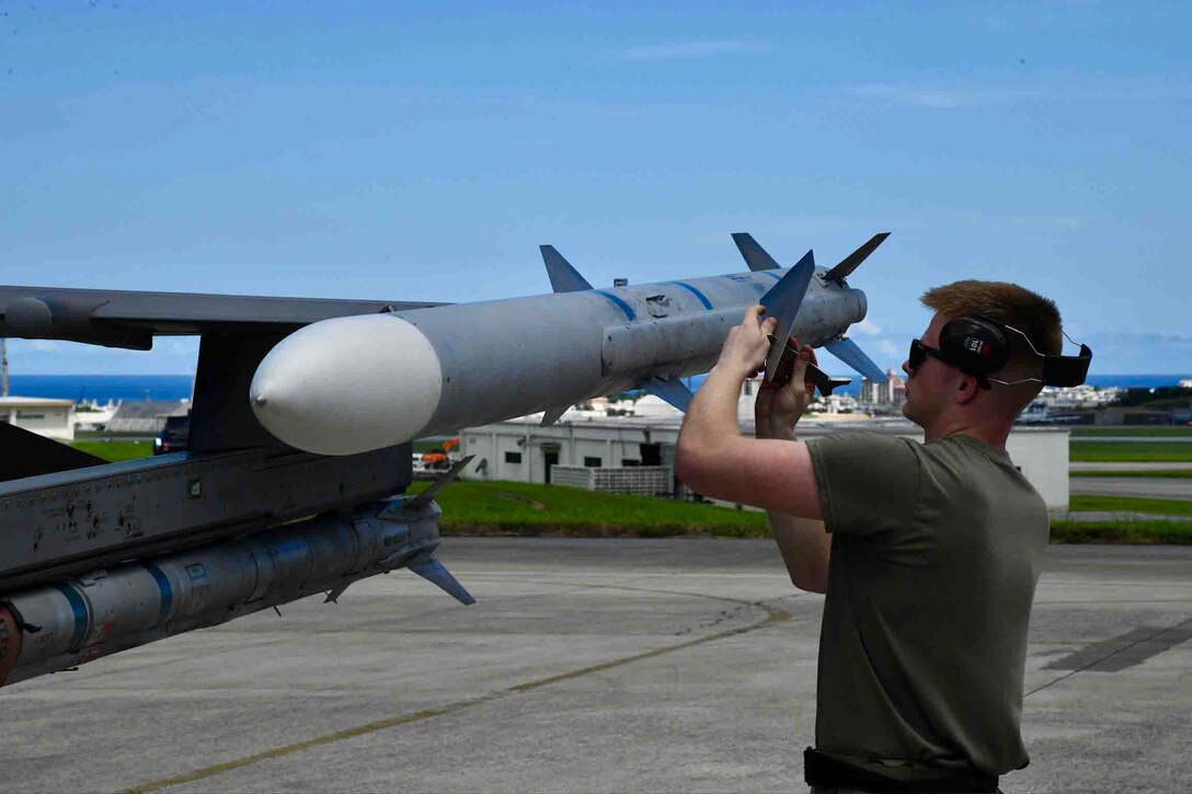 An airman checks a rocket on the wing of an aircraft at a military base.