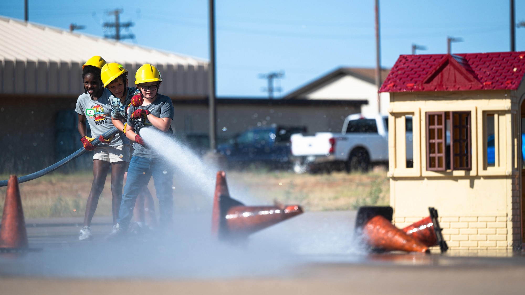Children operate a fire hose during Junior Firefighter Camp at Dyess Air Force Base, Texas, July 16, 2024. Camp participants worked together to knock over cones to simulate putting out a fire. (U.S. Air Force photo by Airman 1st Class Jade M. Caldwell)