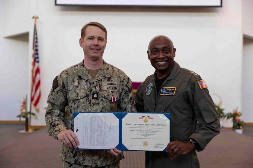 Two sailors stand holding a certificate in a leather folder.