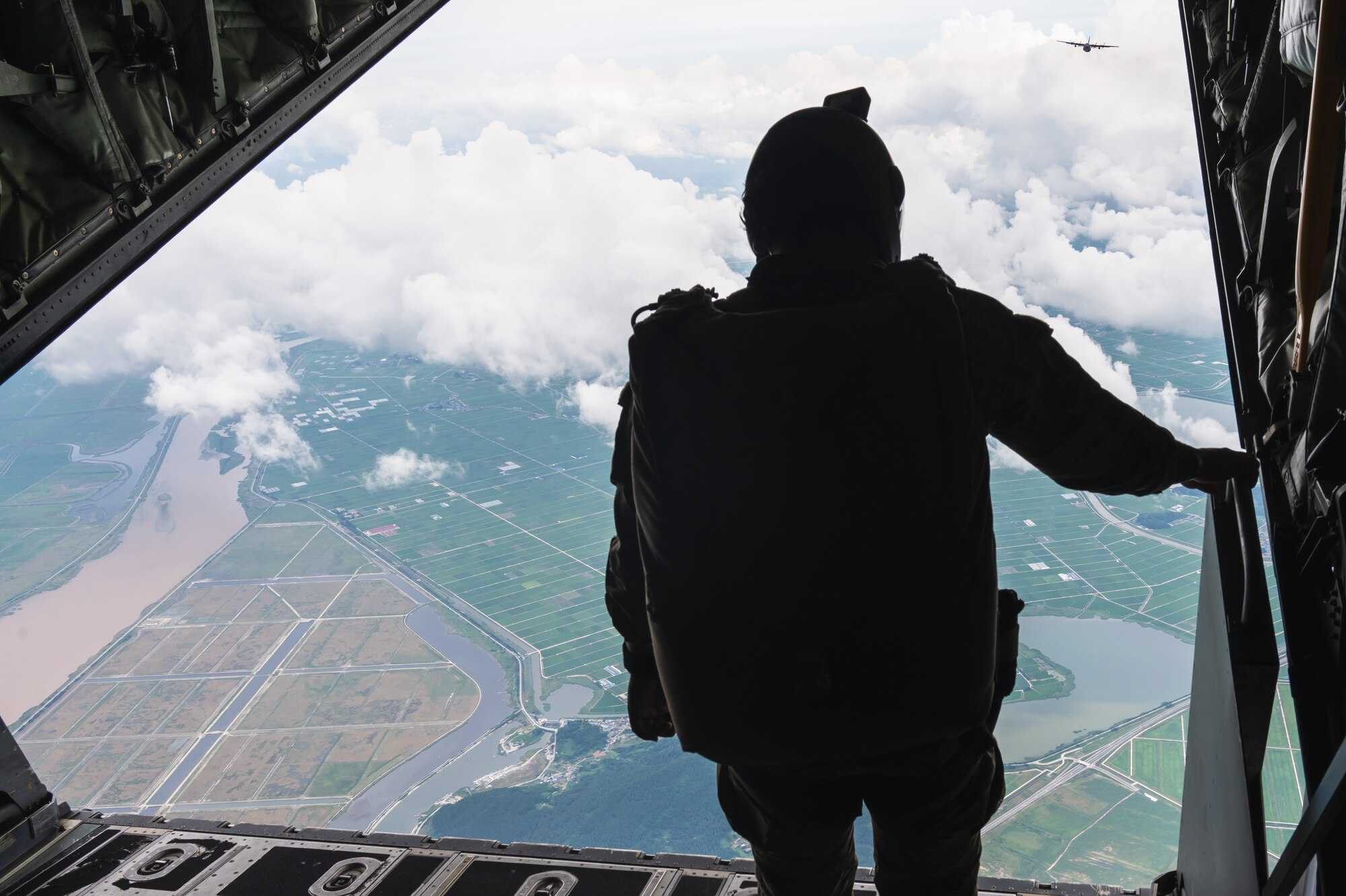 Prior to a military freefall jump, an Airman assigned to the 320th Special Tactics Squadron checks for visual indicators of a drop zone at Kunsan Air Base, Republic of Korea while standing on the back ramp of an MC-130J Commando II aircraft assigned to the 1st Special Operations Squadron.