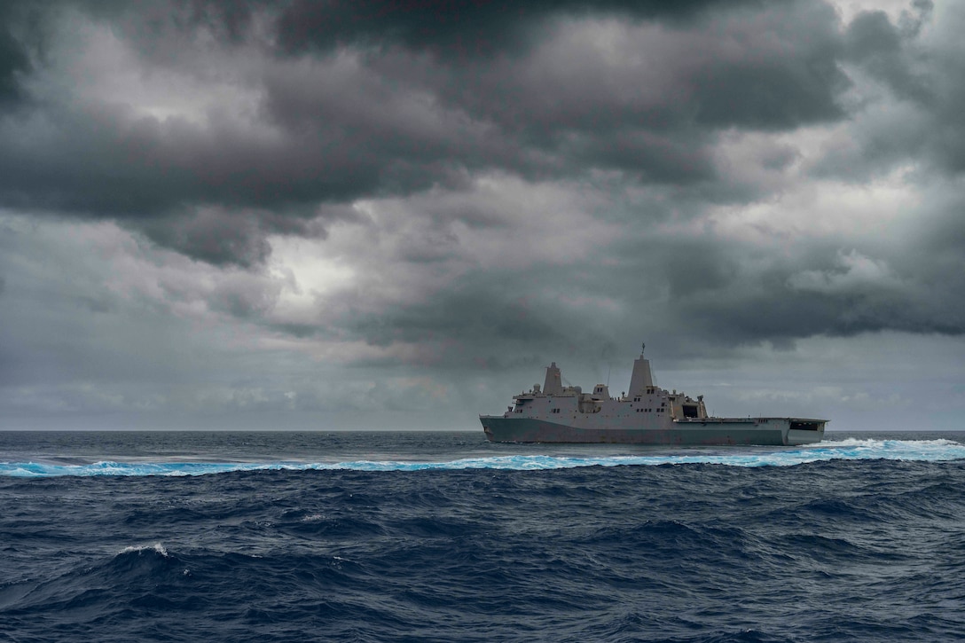 A military ship steams across the ocean on a dark and cloudy day.