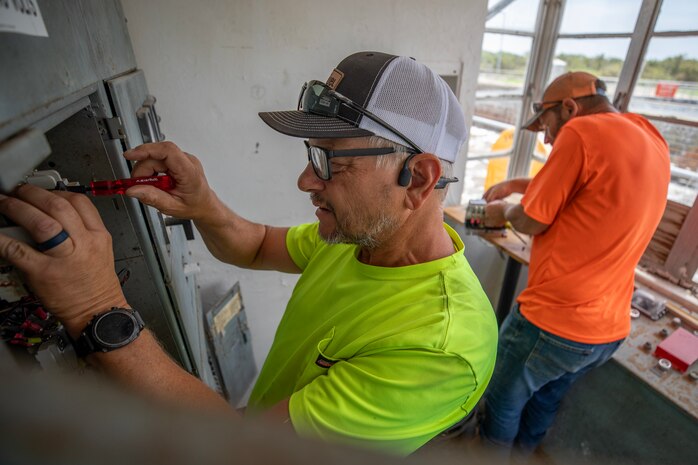 two electricians perform maintenance on an electrical panel