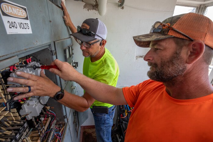 two electricians perform maintenance on an electrical panel