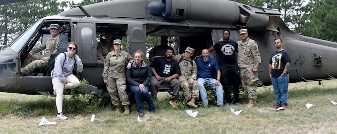 Soldiers in recovery with the Fort Drum SRU stand for a photo with representatives from the Boulder Crest Foundation in front of a training helicopter.