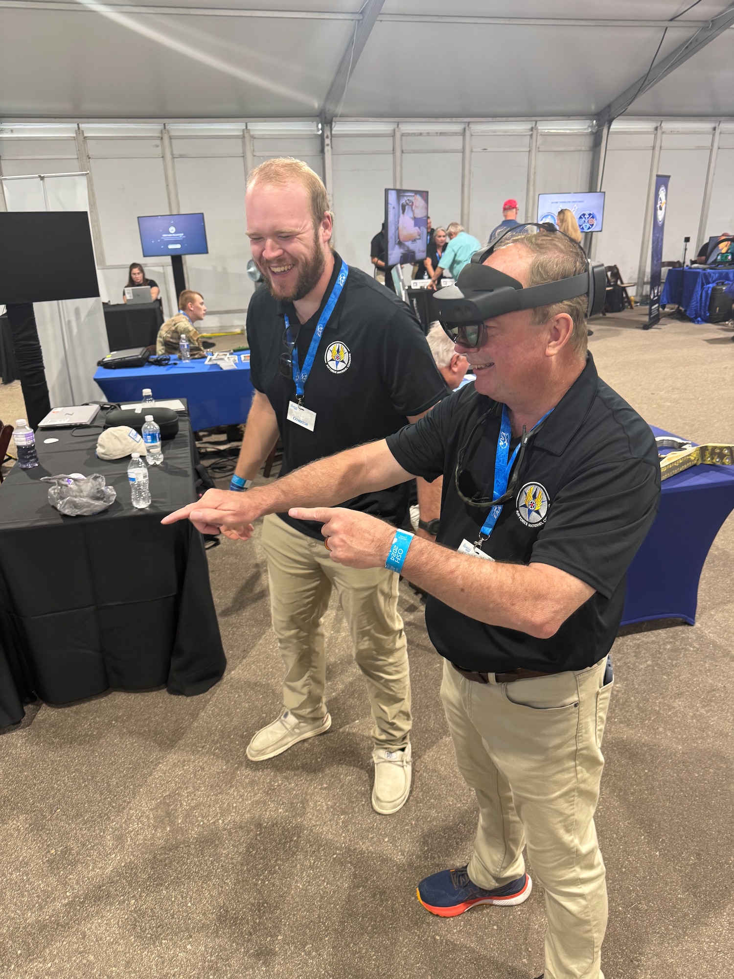 Air Force Sustainment Center Director of Engineering and Technical Management Directorate Wayne Ayer, right, tries out an augmented reality headset with the assistance of Nicholas Jenkins, a mechanical engineer from Warner Robins Air Logistics Complex, left, at the AFSC exhibit during the Experimental Aircraft Association’s AirVenture Oshkosh 2024 airshow in Oshkosh, Wi., July 23. This was the first year that AFMC participated as the featured Air Force major command for this week-long event, which draws in more than 600,000 visitors annually. (U.S. Air Force Photo by Michael Tackitt)
