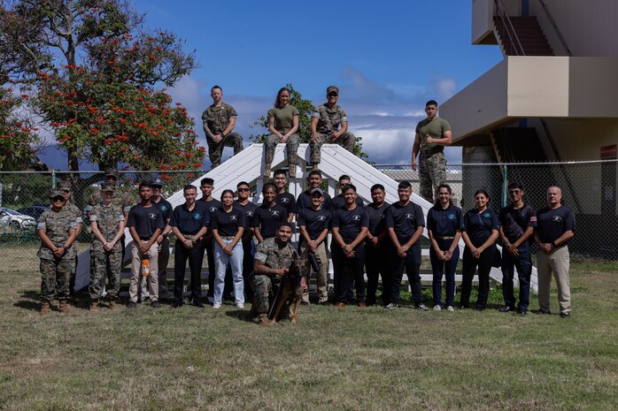 U.S. Marines and students with Kapolei High School’s Marine Corps Junior ROTC pose for a group photo after a K-9 demonstration conducted by Marine Corps Base Hawaii Provost Marshal Office during the Staff  Noncommissioned Officer Academy (SNCOA) Leadership Symposium at MCBH, July 2, 2024. The SNCOA organized its first annual Leadership Symposium, a three-day leadership training focused on promoting community relations and teaching Marine Corps leadership. The symposium included training with KHS’s MC Junior ROTC leadership classes, demonstrations by dog handlers, and a critical-thinking boat activity. (U.S. Marine Corps photo by Lance Cpl. Taylor Von Sanders-Frazer)