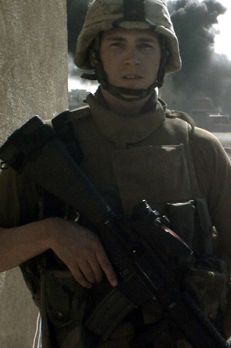 Young Redford poses with M16 riffle while explosion occurs behind him.