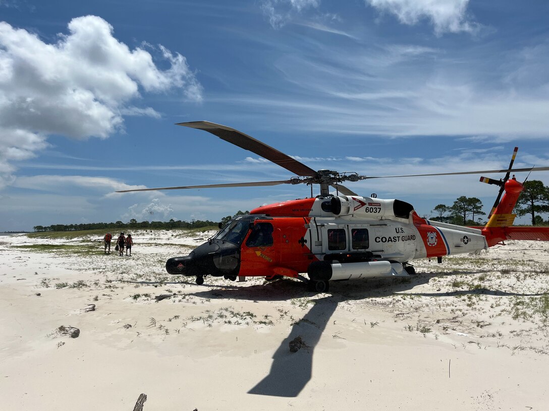 A Coast Guard Air Station New Orleans aviation survival technician walks with two stranded boaters toward a Coast Guard Air Station New Orleans MH-60 Jayhawk helicopter July 29, 2024, on Horn Island, Mississippi. The aircrew arrived on scene, located the two boaters, landed on the beach and brought the two persons aboard the helicopter and safely transported them to Gulfport-Biloxi International Airport. (U.S. Coast Guard video by Coast Guard Air Station New Orleans)