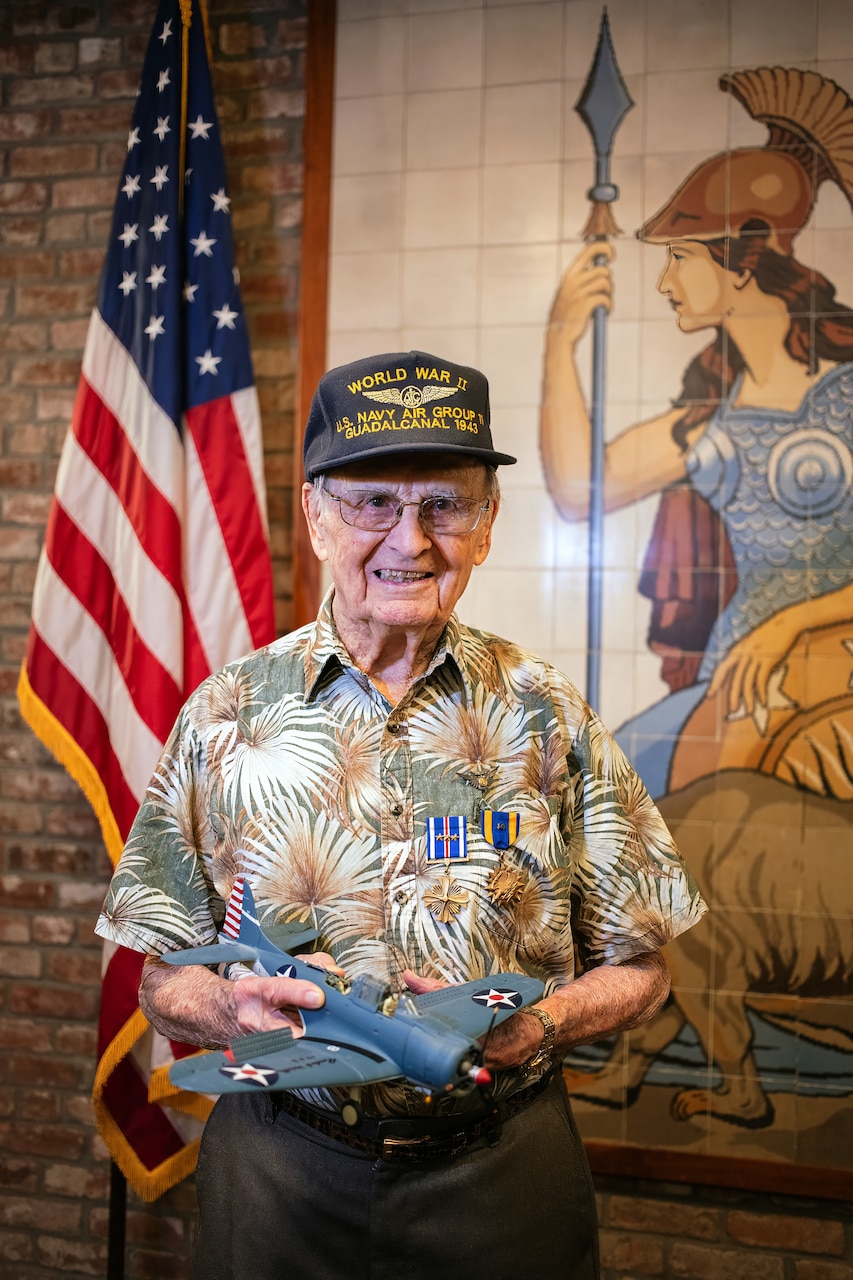 Richard E. “Dick” Miralles poses for a photo wearing his Distinguished Flying Cross and Air Medal, holding a replica of the Scout Bomber Douglas (SBD) Dauntless Dive-Bomber where he earned the awards at the California State Capitol Building, July 25, 2024.